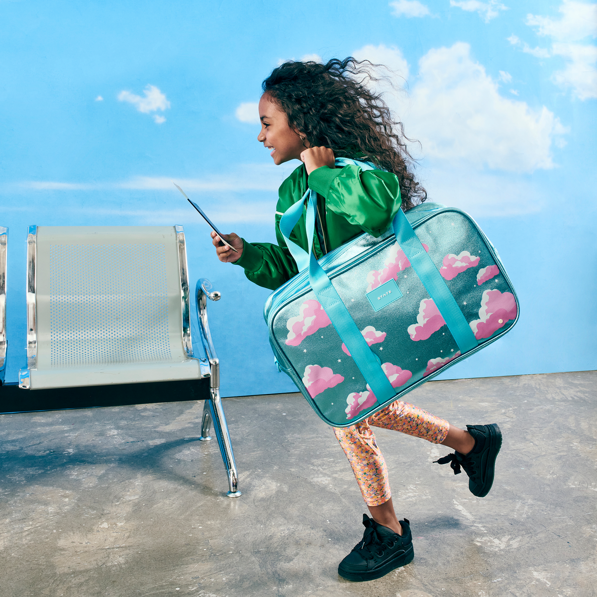 girl running holding STATE Bags Rockaway Duffle Clouds